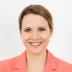 Porträt von Maresa Mayer im korallfarbenen Blazer und zurückgebundenem Haar.